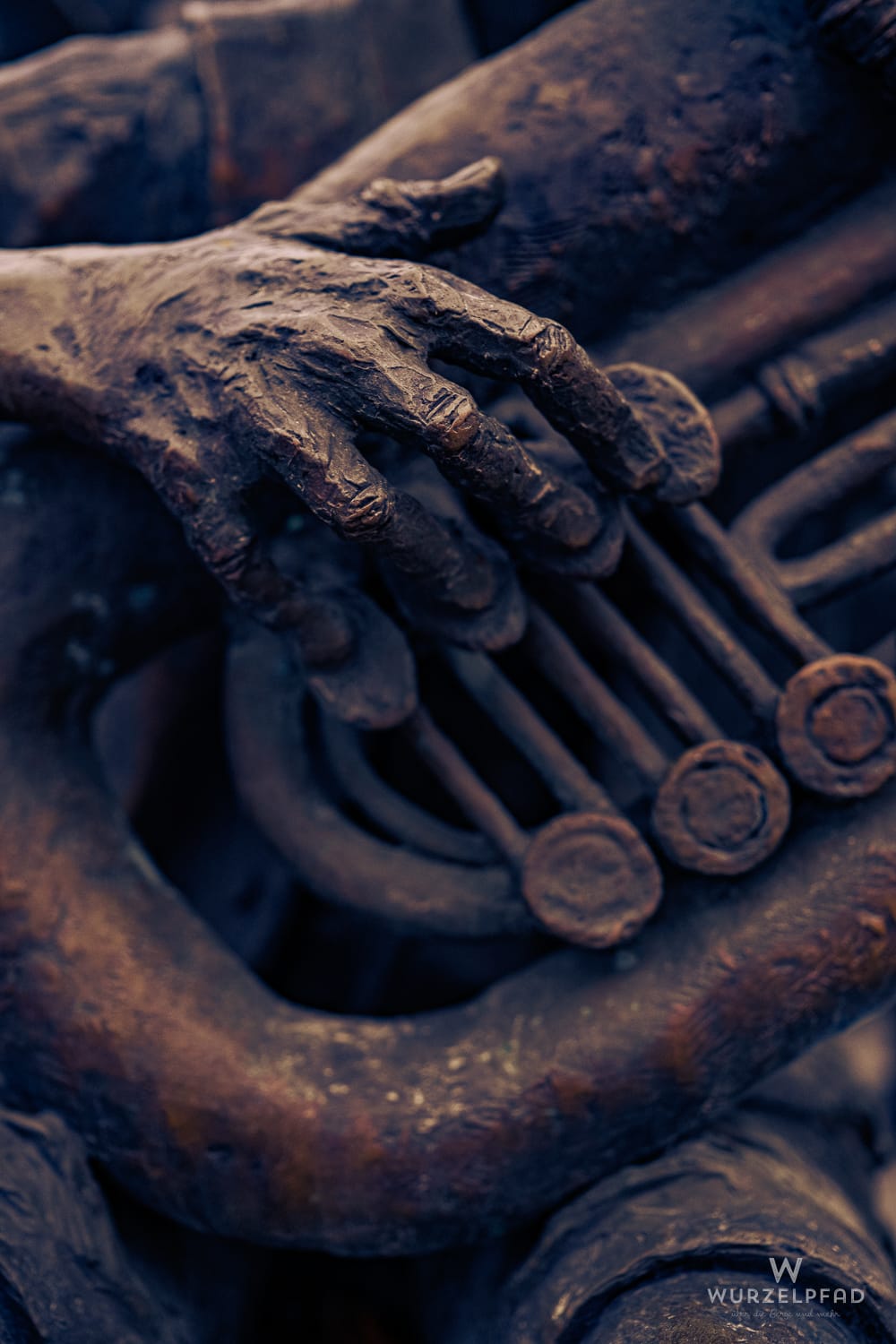 Bronzeskulptur einer Hand, die Tasten eines Saxofons drückt. Detailaufnahme mit rauer, dunkler Metalltextur.