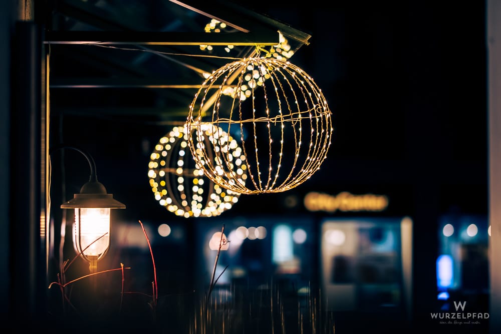 Nachtaufnahme: Eine Laterne und zwei leuchtende Kugeln aus Lichterketten im Vordergrund. Warme Lichter vor dunklem, unscharfem Hintergrund in Deisenhofen.