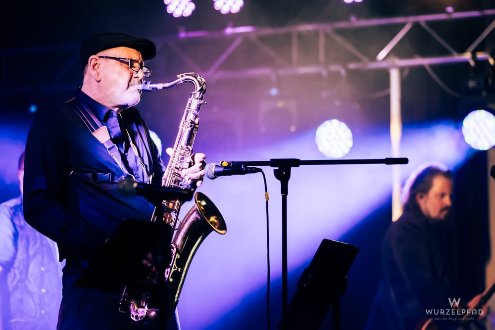 Saxophonist mit Bart, Brille und Mütze spielt auf der Bühne von Beyond – A Pink Floyd Tribute, beleuchtet von lila Scheinwerfern.