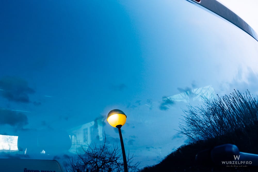 Eine leuchtende Straßenlaterne ragt gegen einen tiefblauen Himmel mit Wolken in der blauen Stunde empor.