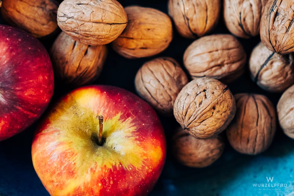 Zwei rote und gelbe Äpfel liegen neben vielen braunen Walnüssen auf einem dunklen Hintergrund.