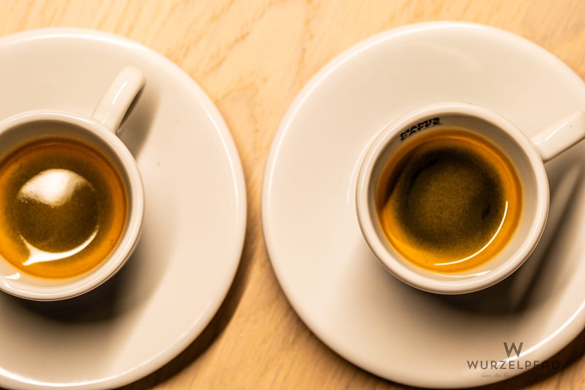 Zwei gefüllte eierschalenfarbene Espressotassen auf einer hellen Tischplatte mit Holzmaserung